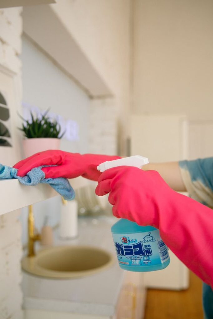 Person using spray bottle and cloth for cleaning a kitchen shelf, ensuring hygiene and cleanliness.